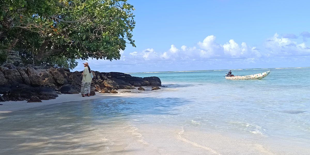 Plage de sable clair au pied d'un rocher, une barque au mouillage